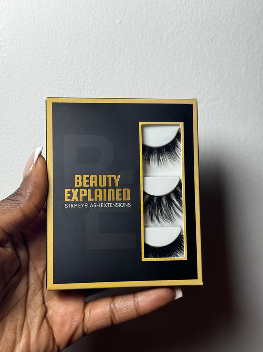 Hand holding a box of 'Beauty Explained' strip eyelash extensions against a white background